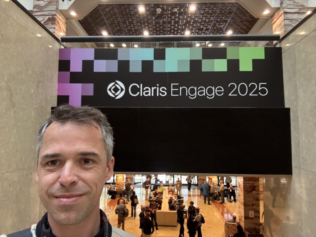 Selfie d'un homme dans un hall, devant l'enseigne « Claris Engage 2025 »